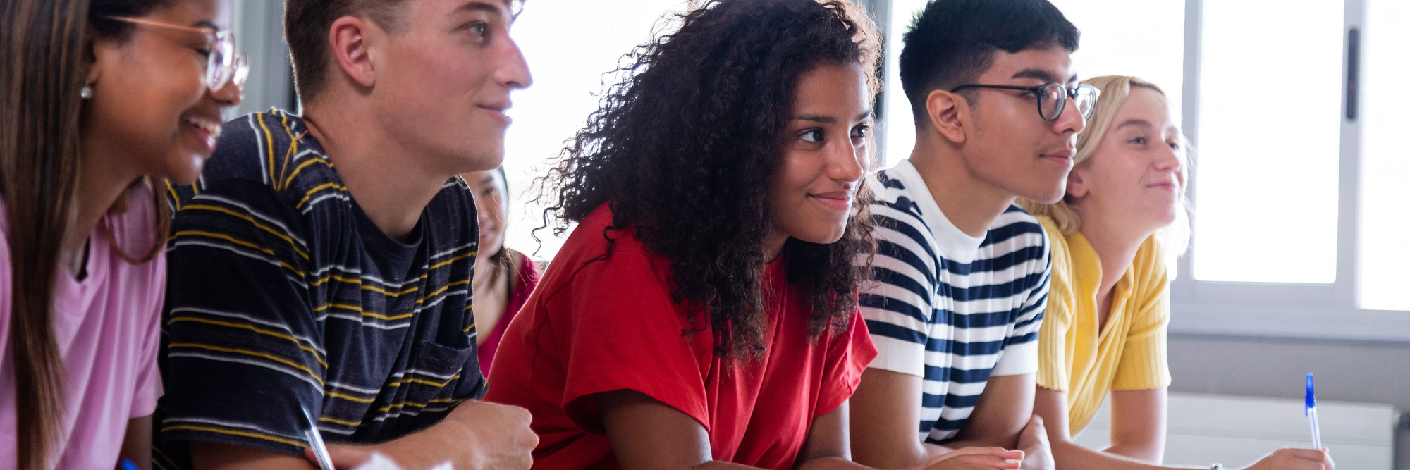close up of a diverse group of students sitting at a table facing the same direction looking intrigued